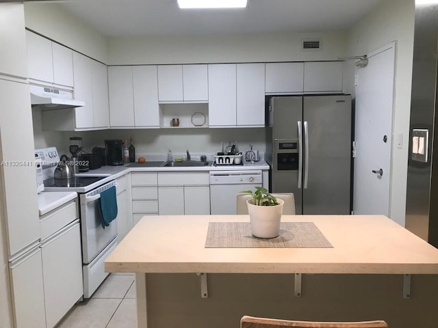 kitchen with white cabinets, light tile flooring, a kitchen breakfast bar, and white appliances