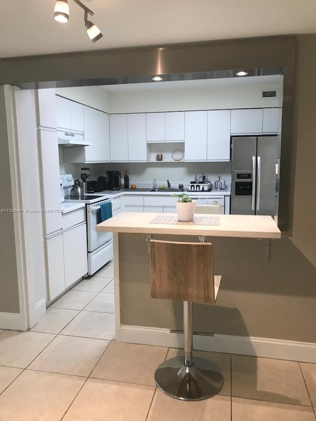 kitchen with white electric range, light tile flooring, a breakfast bar, white cabinets, and stainless steel fridge