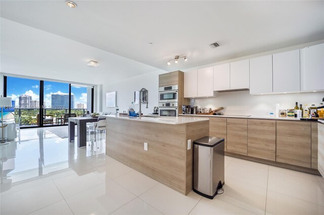 kitchen featuring rail lighting, an island with sink, white cabinetry, and light tile floors