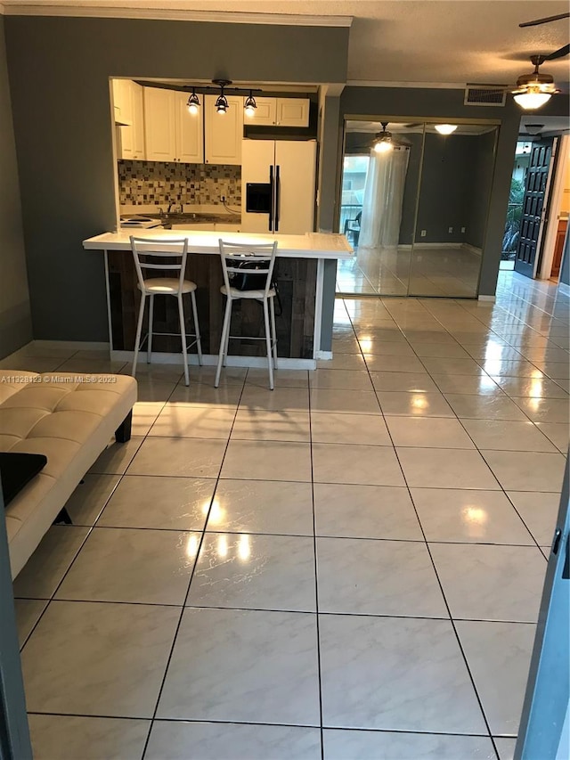 kitchen featuring ceiling fan, tasteful backsplash, white refrigerator with ice dispenser, a breakfast bar, and light tile patterned flooring