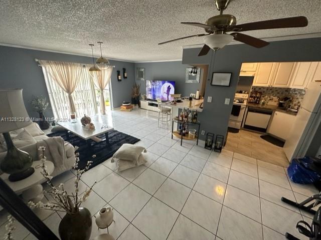 tiled living room featuring ceiling fan, crown molding, and a textured ceiling