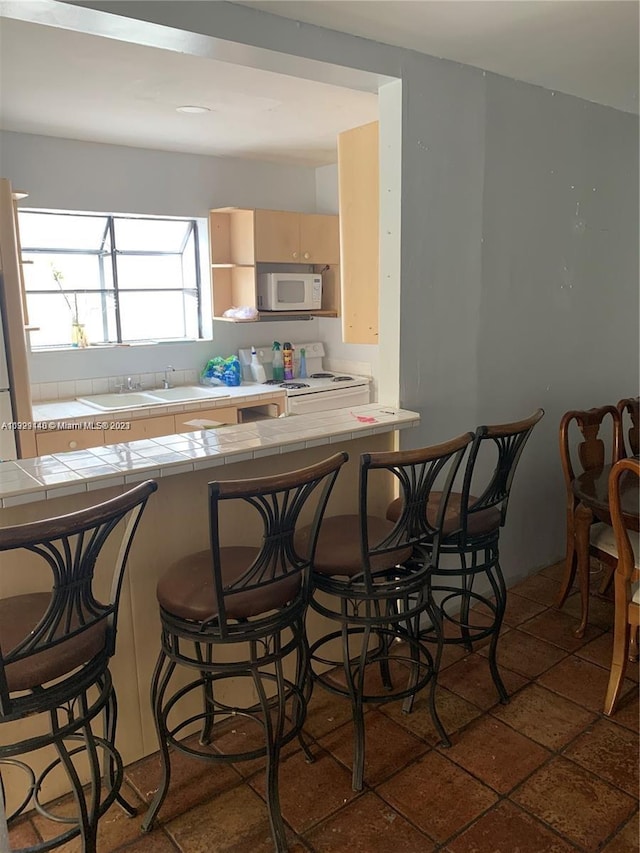 kitchen featuring tile countertops, a kitchen breakfast bar, white appliances, and dark tile flooring