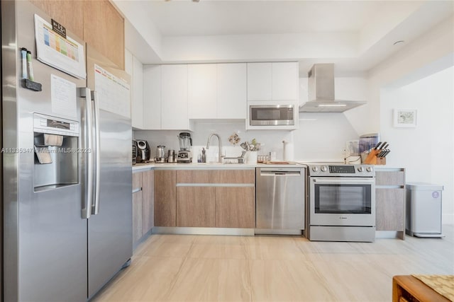 kitchen with stainless steel appliances, light tile floors, wall chimney range hood, white cabinetry, and sink