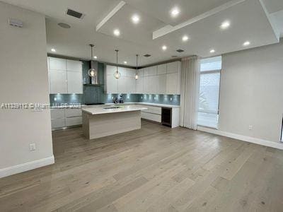 kitchen featuring white cabinets, hanging light fixtures, light hardwood / wood-style floors, and an island with sink