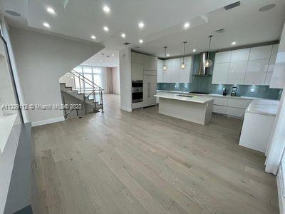 kitchen with exhaust hood, a kitchen island, decorative light fixtures, white cabinetry, and light wood-type flooring