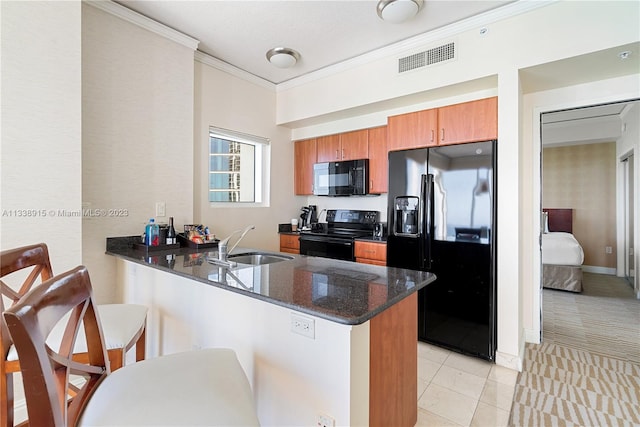 kitchen featuring kitchen peninsula, sink, dark stone counters, black appliances, and a kitchen bar