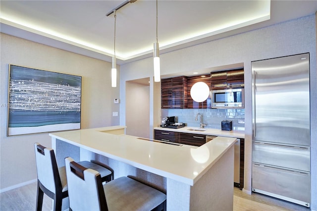 kitchen featuring pendant lighting, built in appliances, a kitchen bar, tasteful backsplash, and light wood-type flooring