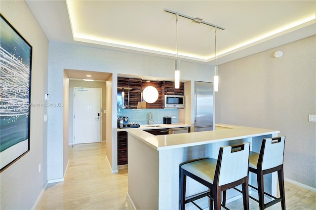 kitchen featuring sink, appliances with stainless steel finishes, a breakfast bar, backsplash, and a tray ceiling