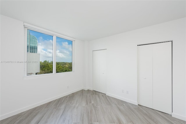 unfurnished bedroom featuring two closets and light wood-type flooring