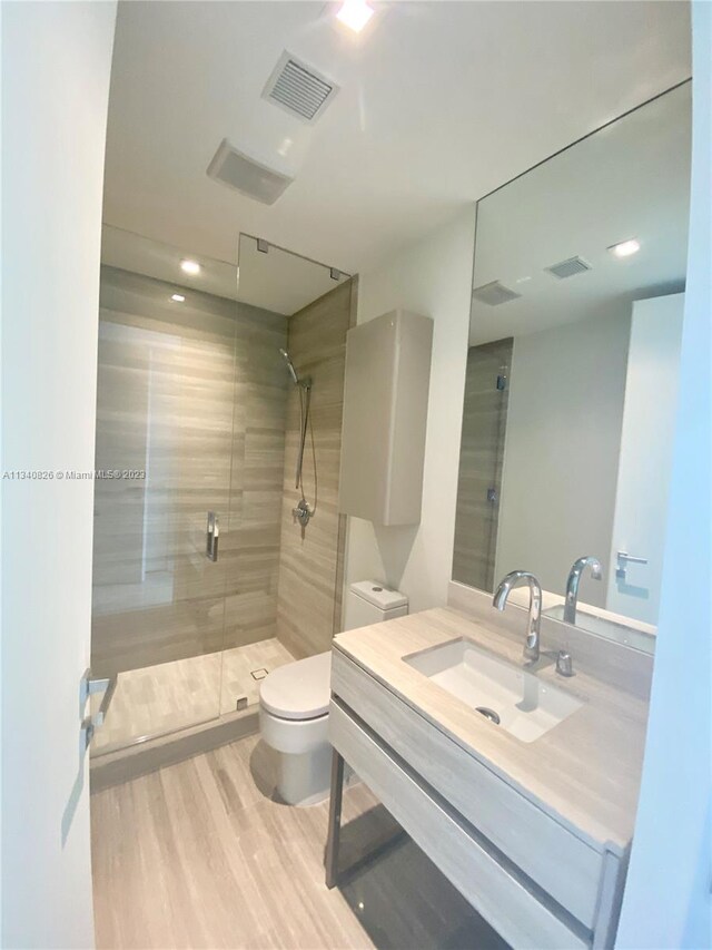 bathroom with walk in shower, vanity, wood-type flooring, and toilet