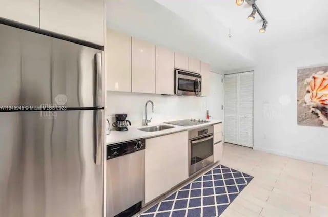 kitchen featuring appliances with stainless steel finishes, white cabinetry, track lighting, and sink