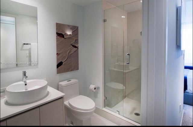 bathroom featuring a shower with door, vanity with extensive cabinet space, and toilet