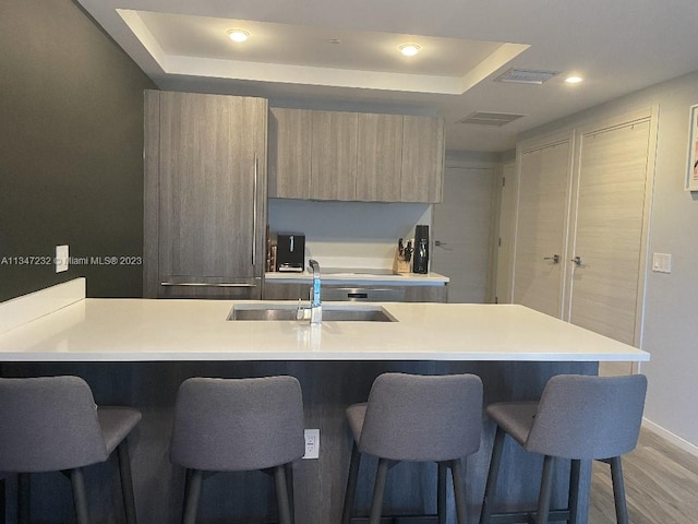 kitchen with a kitchen breakfast bar, a raised ceiling, sink, and light hardwood / wood-style flooring