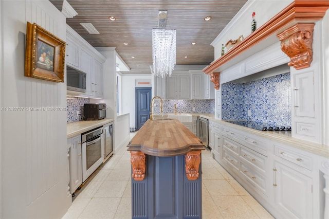 kitchen featuring a kitchen island with sink, appliances with stainless steel finishes, backsplash, wood counters, and a notable chandelier