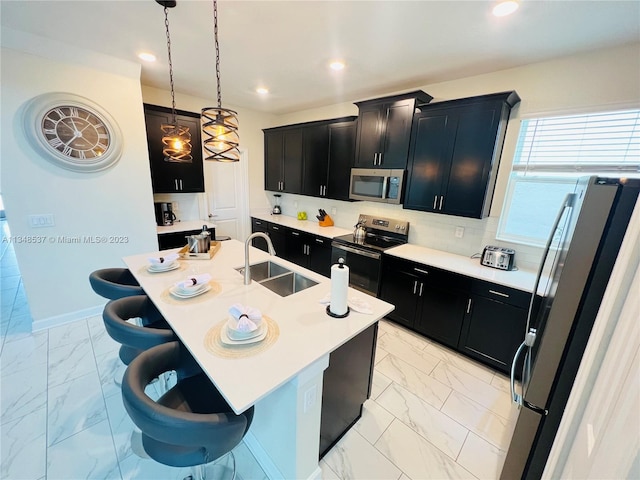 kitchen with sink, an island with sink, stainless steel appliances, decorative light fixtures, and a breakfast bar