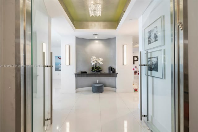 hall with light tile floors, a tray ceiling, and a notable chandelier