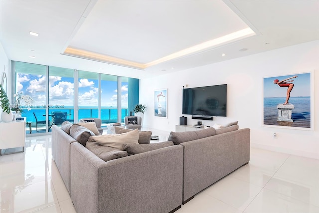 tiled living room featuring a raised ceiling, a water view, and expansive windows