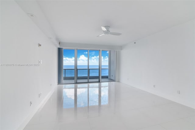 tiled empty room featuring ceiling fan and a water view