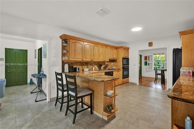 kitchen featuring a kitchen bar, light tile flooring, dark stone countertops, and black appliances