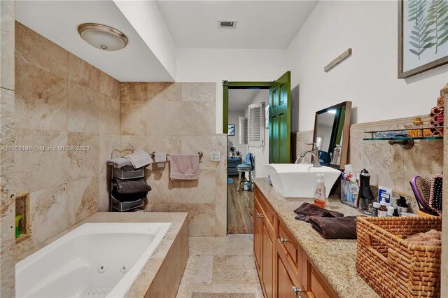 bathroom with tile walls, tile floors, tiled bath, and vanity