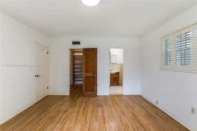 unfurnished bedroom with connected bathroom, light hardwood / wood-style floors, a closet, and crown molding