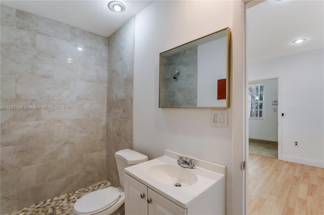 bathroom with oversized vanity, wood-type flooring, toilet, and tiled shower