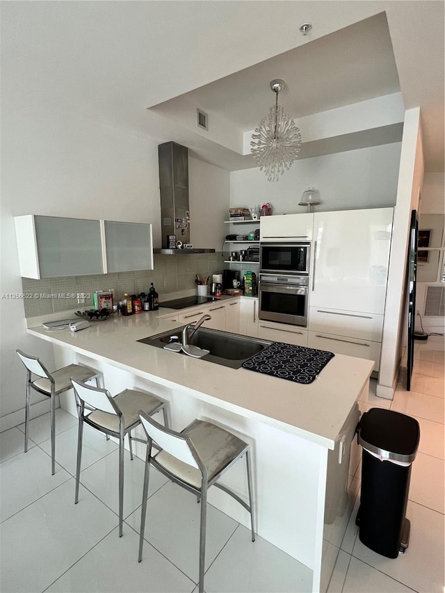 kitchen featuring a kitchen breakfast bar, a notable chandelier, built in microwave, white cabinetry, and oven