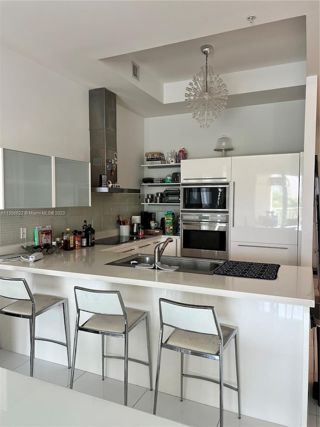 kitchen with oven, backsplash, an inviting chandelier, a kitchen bar, and white cabinets