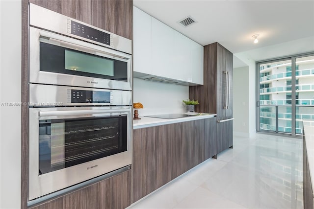 kitchen featuring plenty of natural light, double oven, light tile floors, black electric stovetop, and white cabinets