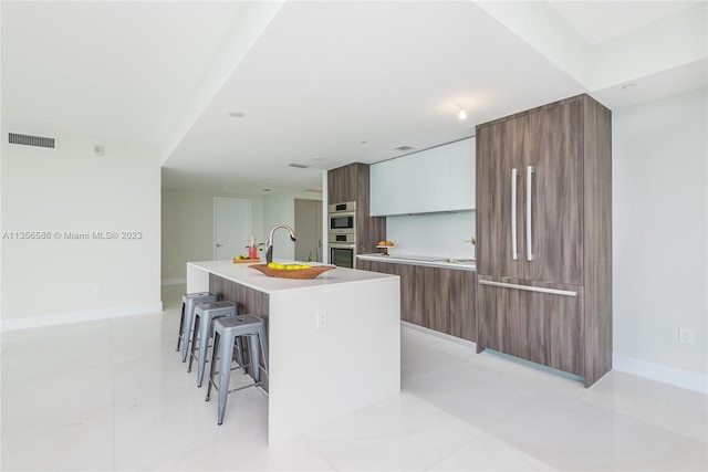 kitchen with an island with sink, a kitchen bar, white cabinets, and light tile floors