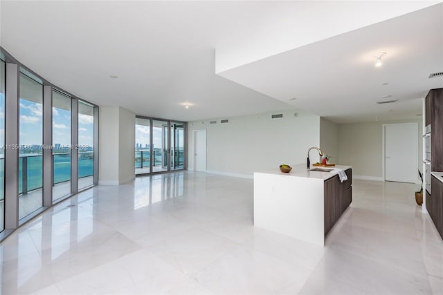 kitchen with a wall of windows, light tile floors, a kitchen island with sink, and sink