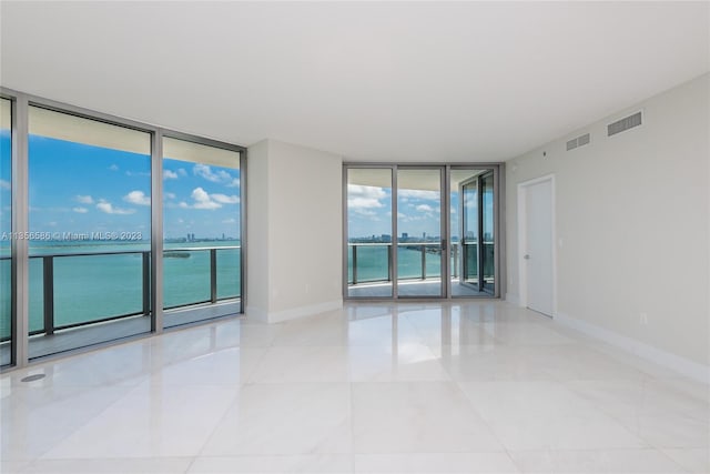 tiled spare room featuring a water view, a wall of windows, and a wealth of natural light