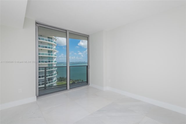 spare room with a water view, a wall of windows, and light tile floors