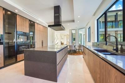 kitchen featuring light tile patterned flooring, a large island, wall chimney exhaust hood, and sink