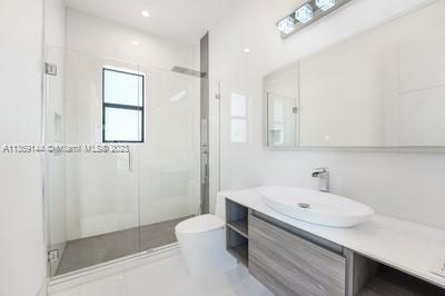 bathroom with tile patterned floors, a shower with door, vanity, and toilet