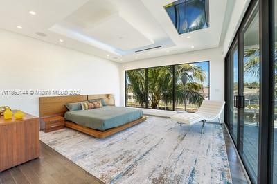 bedroom featuring hardwood / wood-style flooring, access to exterior, multiple windows, and a tray ceiling