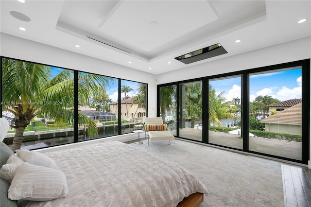 bedroom with hardwood / wood-style floors, a water view, access to outside, and a tray ceiling