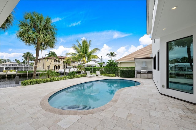 view of pool featuring an outdoor kitchen, a water view, and a patio