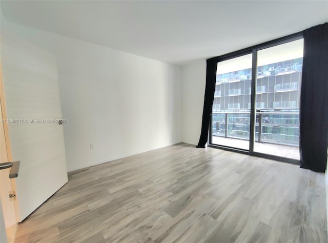 empty room with floor to ceiling windows and light hardwood / wood-style flooring