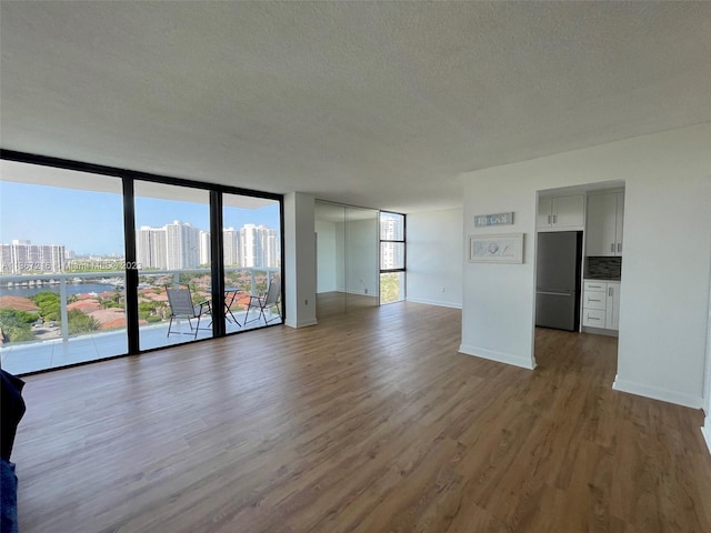 unfurnished living room featuring a wall of windows, hardwood / wood-style floors, and a textured ceiling