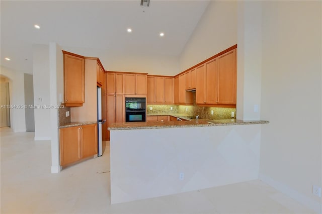 kitchen with light stone countertops, kitchen peninsula, backsplash, black double oven, and high vaulted ceiling