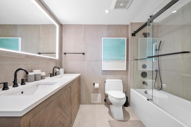 full bathroom with tile walls, toilet, double sink, tile flooring, and shower / bath combination with glass door