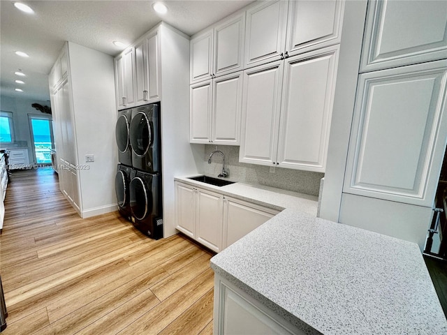 kitchen with stacked washer / dryer, sink, white cabinets, and light hardwood / wood-style flooring