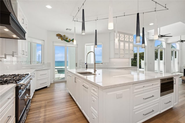 kitchen featuring pendant lighting, premium range hood, ceiling fan, backsplash, and a kitchen island with sink