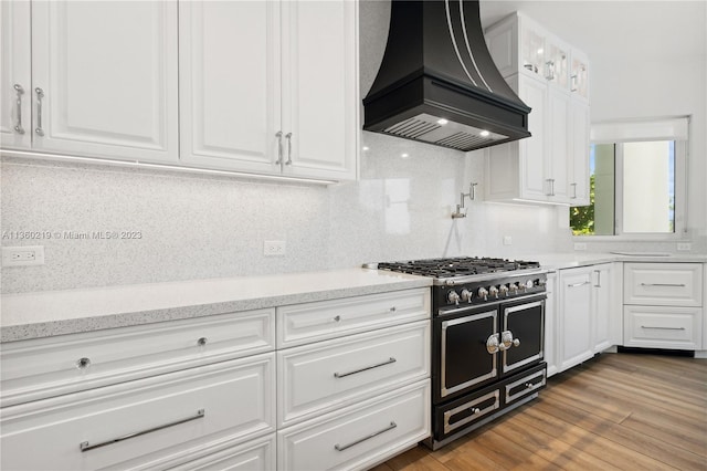 kitchen with custom range hood, backsplash, double oven range, wood-type flooring, and white cabinetry