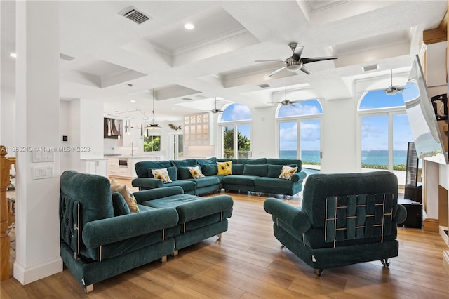 living room featuring coffered ceiling, ceiling fan, light hardwood / wood-style flooring, crown molding, and a water view