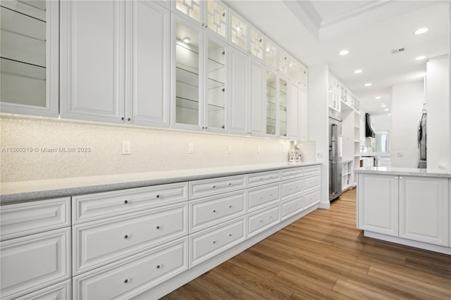 kitchen featuring refrigerator, white cabinets, backsplash, light hardwood / wood-style floors, and light stone countertops