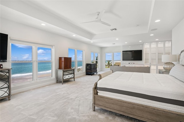 bedroom with a water view, a tray ceiling, ceiling fan, and light colored carpet