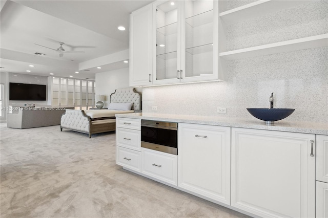 kitchen featuring ceiling fan, sink, light stone counters, white cabinets, and light carpet