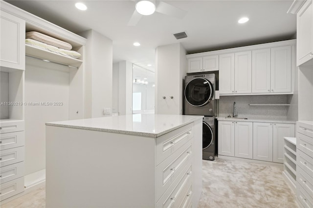 kitchen featuring stacked washer and dryer, ceiling fan, sink, white cabinets, and light stone counters